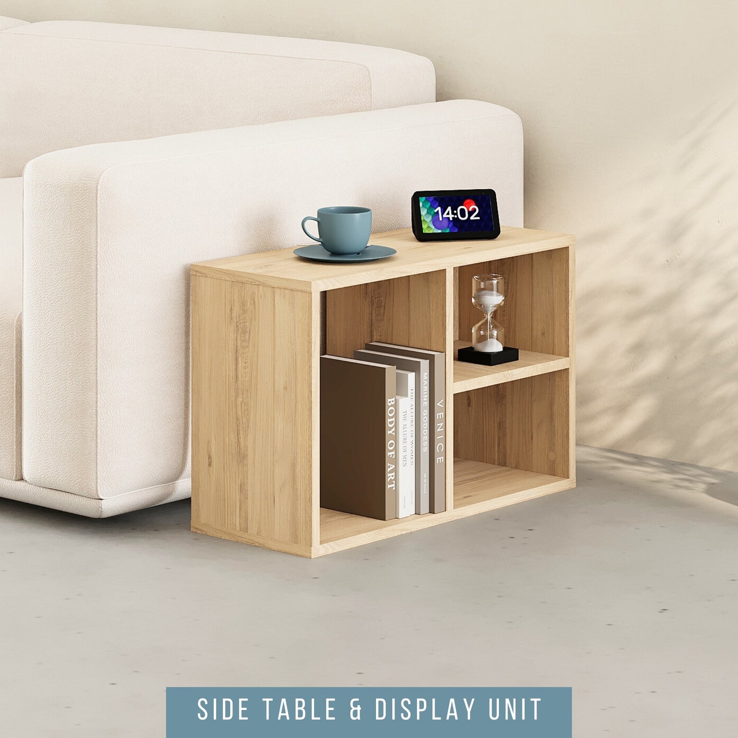 Wood-effect shelving unit used as a side table next to a cream sofa. The unit features multiple compartments holding books and a small hourglass. The top surface displays a cup and saucer along with a digital clock on the side table