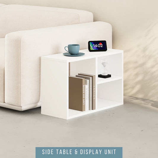 A white modular shelving unit placed next to a sofa, functioning as a side table with a cup on top and a display unit with a framed picture and books.